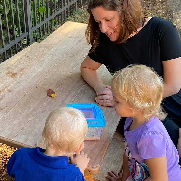 Montessori teacher Ms. Julie observes two students studying a frog.